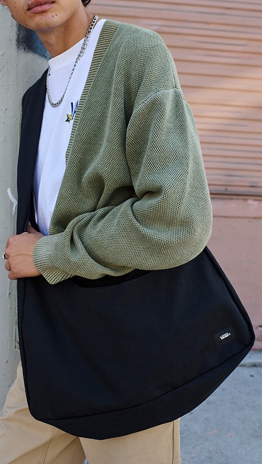 A close-up of a man wearing a green Vans cardigan and black Gotsman Messenger Bag.