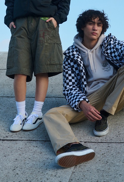 A young woman poses on a roof wearing a black hoodie, green cargo shorts, and marshmallow white Super Lowpro.