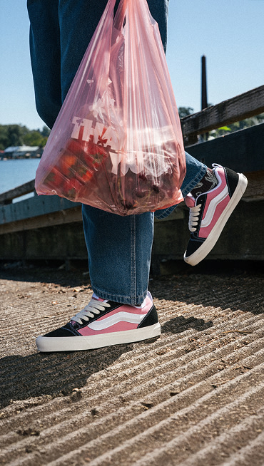 A knee-down shot of someone wearing pink and black Knu Skool with blue jeans on a boat ramp near the water.