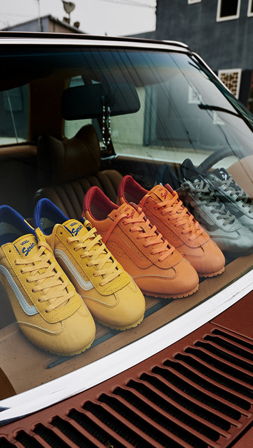 A yellow pair, a gunmetal gray pair, and a solar orange pair of Premium Super Lowpro rest on the dashboard of a car under a foggy sky.
