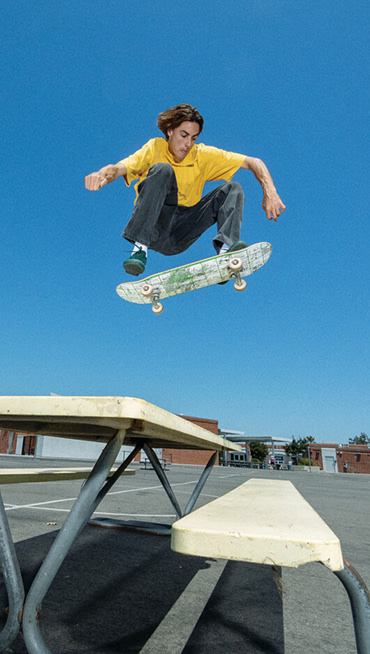 Vans Skate Team Rider Curren Caples jumping over a playground table wearing green Curren shoes from the United Through Skateboarding collection.