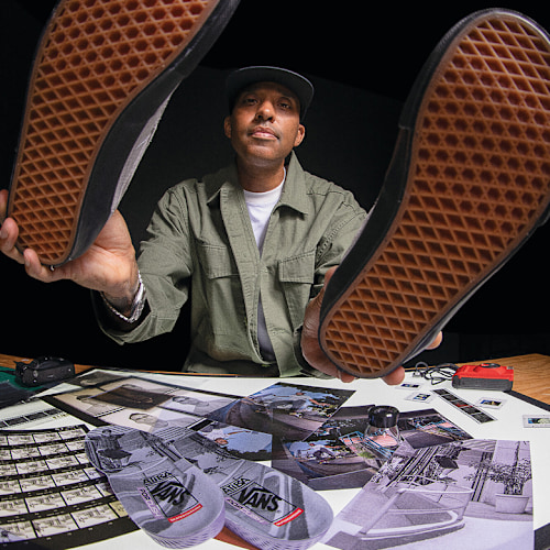 Atiba holds up two shoes from the United Through Skateboarding collection over photographs on a work table.