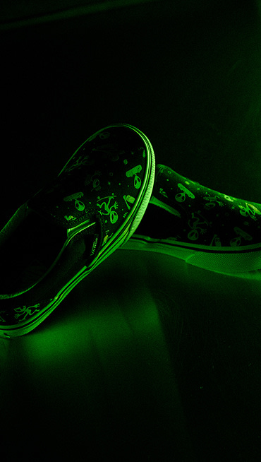 Close-up on the glow-in-the-dark aliens on the Little Kids Classic Slip-On Shoe under an eerie green light for Halloween.