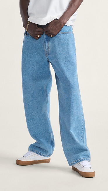A waist-down shot of a young man wearing blue Check-5 Baggy Denim Pants with white Old Skool in a photography studio.