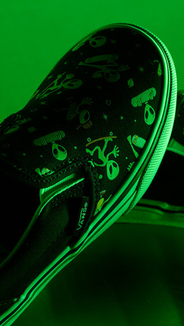 Close-up on the glow-in-the-dark aliens on the Little Kids Classic Slip-On Shoe under an eerie green light for Halloween.