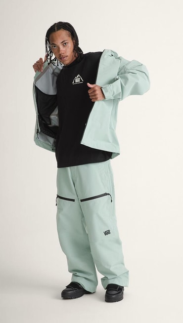 A young man puts on his powder blue Hi-Country Snow Jacket and Hi-Country Snow Pants in a photography studio.