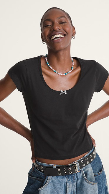 A waist-up shot of a woman smiling at the camera wearing a black Checkerboard Bow Scoop T-shirt.