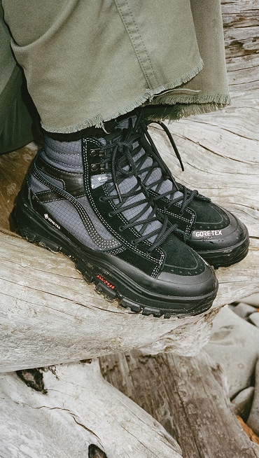 A close-up of someone wearing the black Sk8-Hi GORE-TEX on a log.