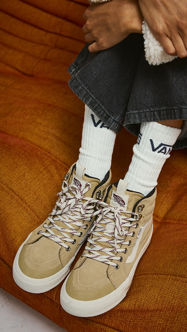 A close-up of someone wearing the tan and white waterproof and insulated Sk8-Hi GORE-TEX on a felt sofa.