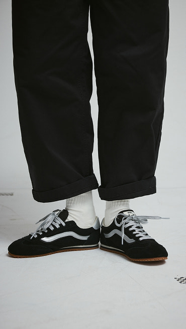 A knee-down shot of someone wearing black Super Lowpro with black jeans and white Vans crew socks.