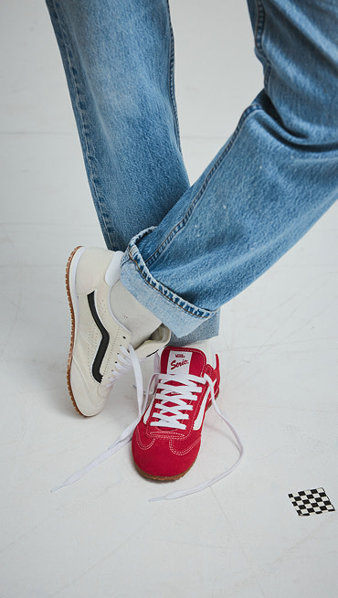 A knee-down shot of someone wearing a marshmallow white Super Lowpro on one foot and a racing red Super Lowpro on the other with blue jeans.