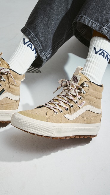 Close-up of someone wearing tan Sk8-Hi Insulated shoes with black jeans and white Vans crew socks.