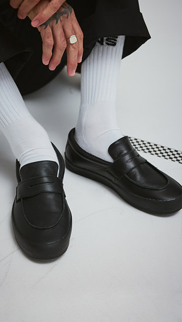 A young man wearing black Skate Loafer paired with white crew socks and black pants.