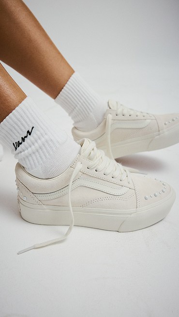 Close-up of the white Old Skool Pearlized paired with white Vans script logo crew socks in a photography studio.