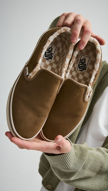 A young man holds up the high pile fleece lining of the Classic Slip-On.