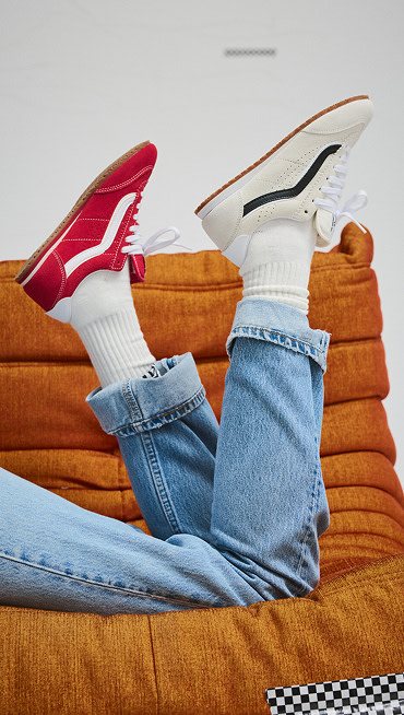 Someone lying on an orange sofa wearing a marshmallow white Super Lowpro on one foot and a racing red Super Lowpro on the other with blue jeans.