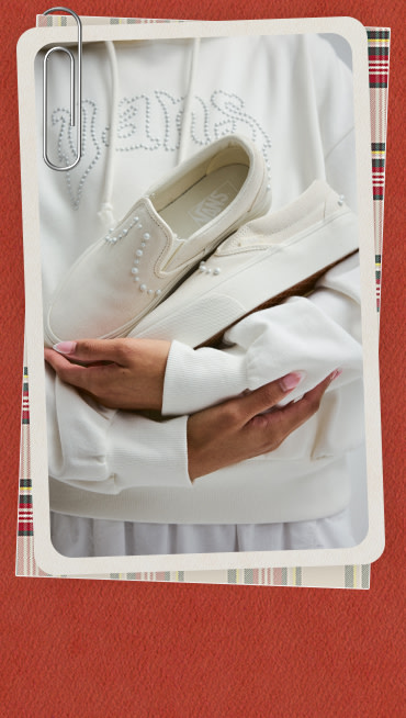 A red holiday border around an image of a young woman holding white Classic Slip-On Pearlized in a white Pearls Logo Retro Pullover Sweatshirt.