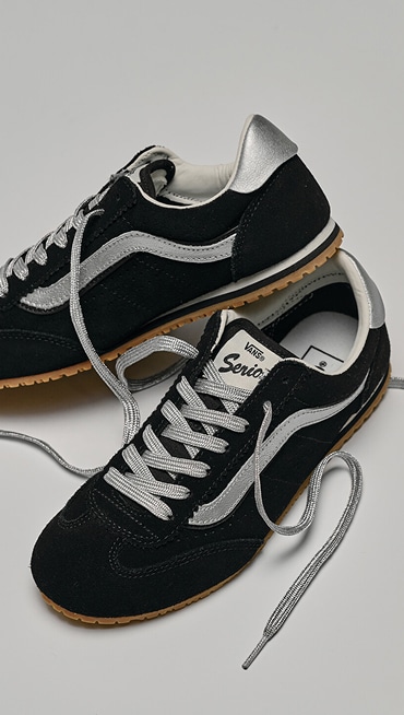 A pair of black and silver Super Lowpro lie on the floor of a photography studio with their laces undone.