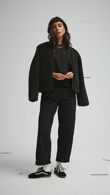 A young woman poses in a photography studio wearing black and silver Super Lowpro and an all-black outfit.