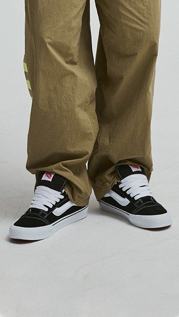 A waist-down shot of a young man wearing black and white Knu Skool with Ronnie Track Pants.