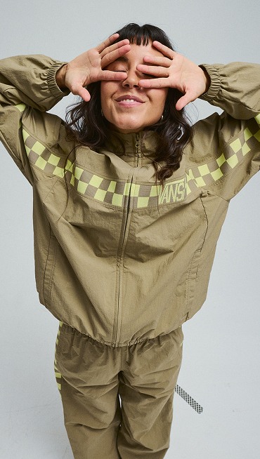 A young woman puts her hands over her face wearing the yellow and brown Ronnie Track Jacket and Pants in a photography studio.
