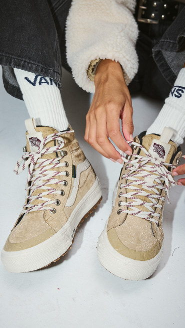 Close-up of someone lacing up tan and white Sk8-Hi GORE-TEX Insulated shoes on the floor of a photography studio.