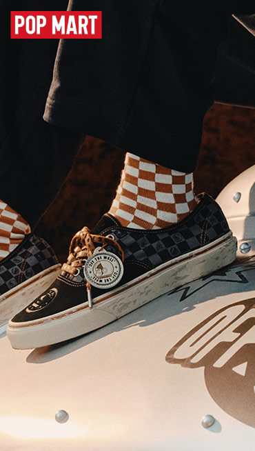 A young man poses on an orange sofa wearing black and white Authentic, blue jeans, and a red Blur Drop Long Sleeve T-Shirt.