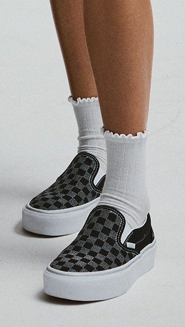 Close-up on the Checkerboard black colorway of the Classic Slip-On Platform Checkerboard paired with white frilly socks.