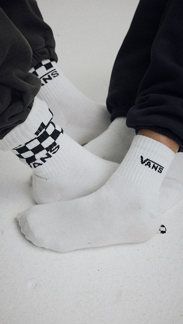 Close up of two people's feet wearing socks. One is wearing, Classic Check Crew Socks in White. The other is wearing Classic Half Crew Socks in White.