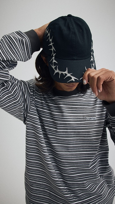 Image of a person wearing a Thorn Jockey Hat and a Wesley Stripe Long Sleeve Knit Shirt in a grey photography studio.