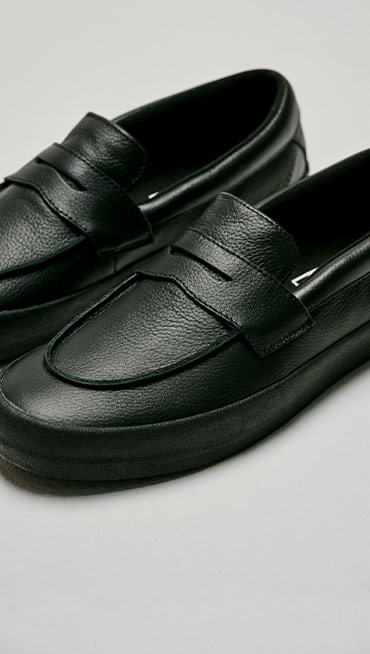 Image of Skate Loafers in all-black sitting on the floor of a grey photography studio.