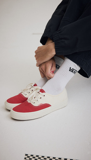 Medium shot of someone sitting on the floor of a grey photography studio wearing a pair of the Authentic Shoe in Racing Red with Classic Crew Socks in White.