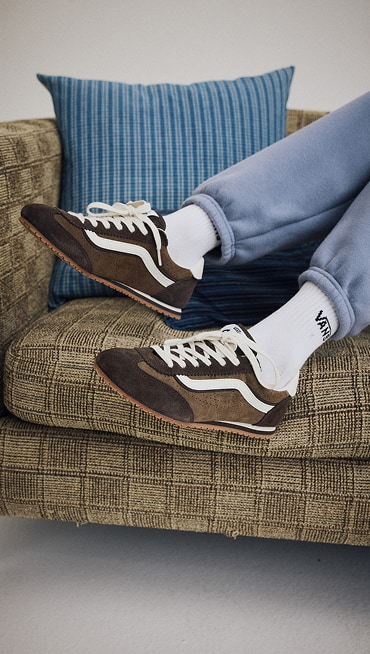 Close up of a woman wearing the Super Lowpro in Demitasse Brown while kicking up her feet on a checkered couch.