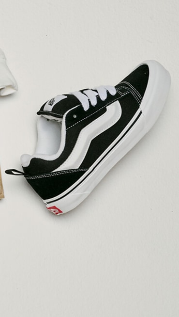 Close up of a single Little Kids Knu Skool Shoe in Black / White on the floor of a grey photography studio.