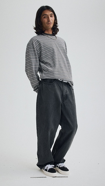 Man in a grey photography studio wearing a white shirt and Check-5 Loose Denim Pants in Stonewash Blue.