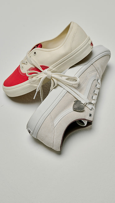 A pair of red and white Authentic shoe with its laces tied to a beige Old Skool shoe on the floor from the Vans Valentine’s Day Collection.