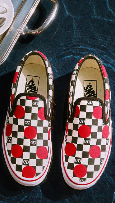 Close up of a pair of the Classic Slip-On Valentino Shoe sitting on water with a silver tray and a cup of coffee with a silver spoon on it in the upper left corner.