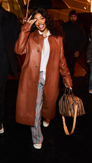 Singer and Vans Artistic Director SZA walks down a street wearing Authentic, striped slacks, and a brown leather trench coat.