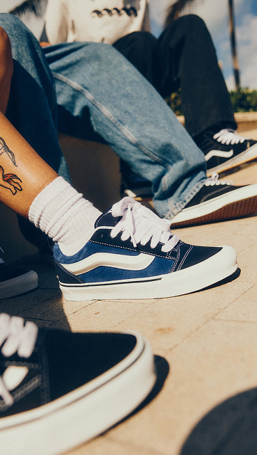 A low angle shot of four people each wearing different low top Vans shoes. The image is zoomed in on their legs.