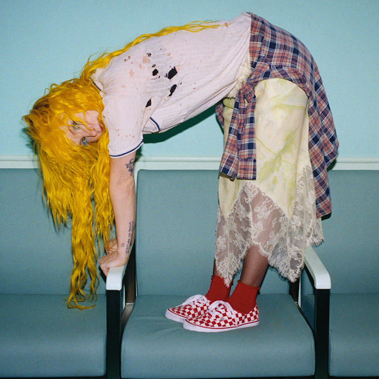 Paramore singer Hayley Williams in tattered clothes bending over a chair wearing red Checkerboard Authentic.