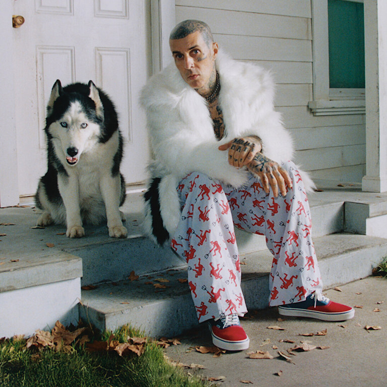 Blink-182 drummer Travis Barker sits next to a husky in a fuzzy white jacket wearing red and blue Authentic from the Worn Loud Authentic Legacy drop.