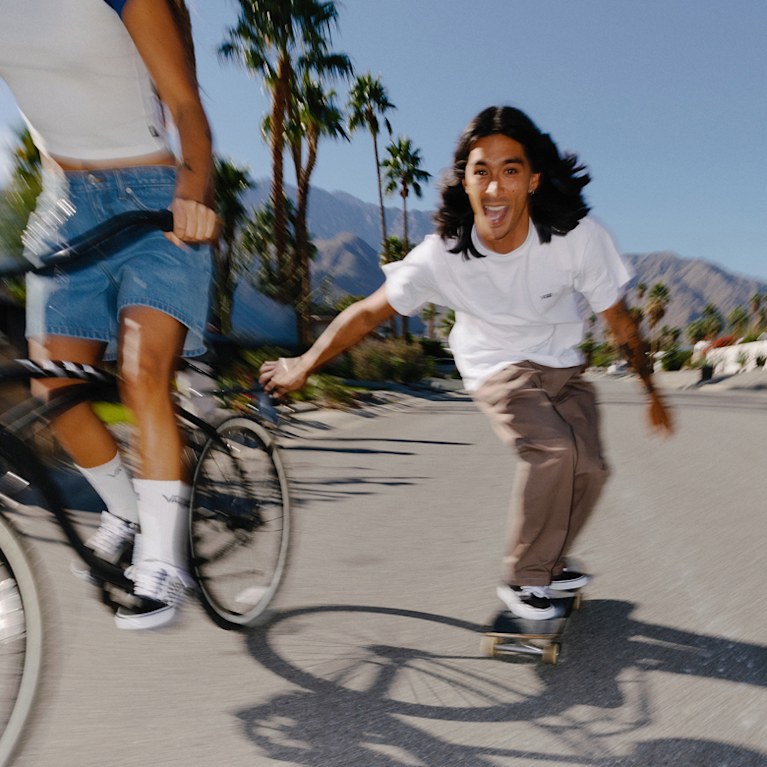 A blurry image of a young man skating on a sunny day in Vans shoes and clothes.
