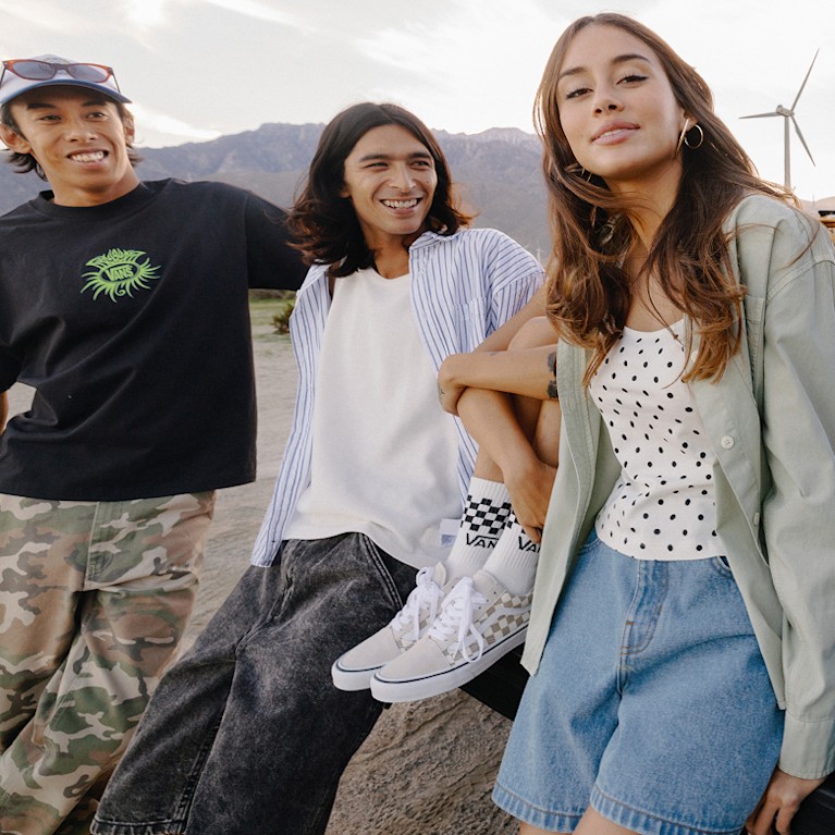 Un groupe d’amis assis sur le plateau d’un camion dans le désert au crépuscule. Tout le monde porte des chaussures et des vêtements Vans.