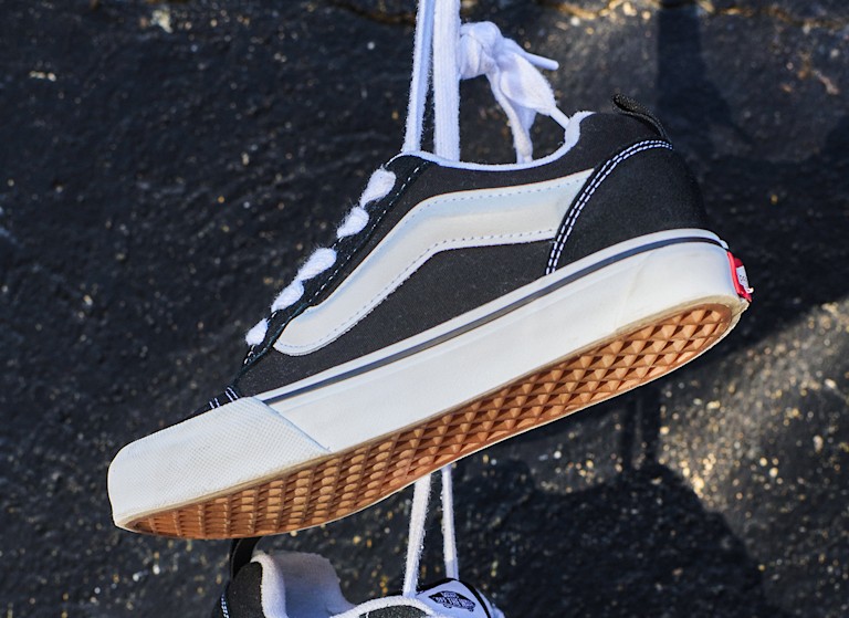 A close-up of a pair of black and white Knu Skool hanging by their laces.