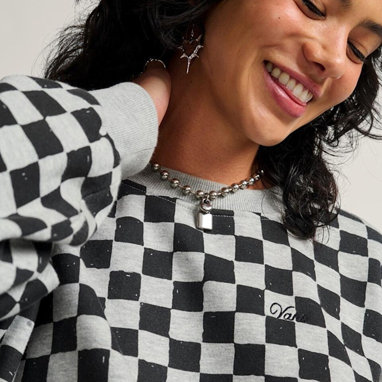 A close-up of a woman smiling and posing in a gray and black Checkerboard pullover.