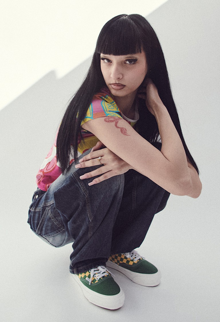 A close-up of a woman in a photography studio squatting and wearing dark jeans and Fairway Green and Yellow Premium Authentic Checkerboard Shoe.