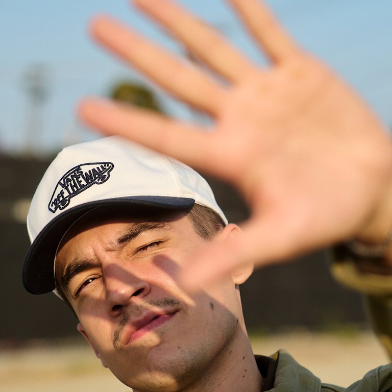 A man tries to block out the sun with his hand wearing a white “Off the Wall” logo hat.