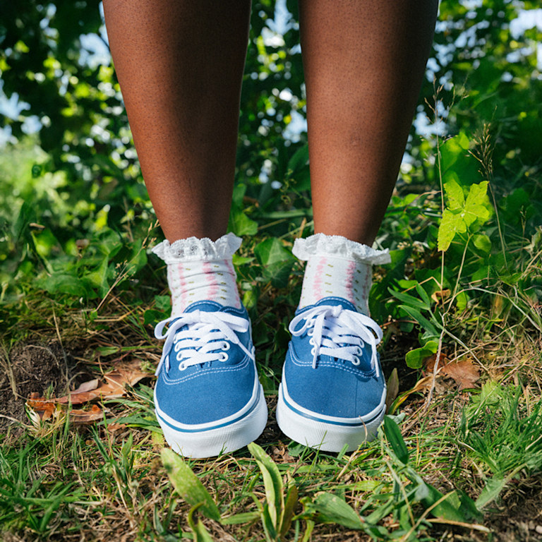 A close-up of someone wearing blue Authentic with frill socks on some grass on a sunny day.