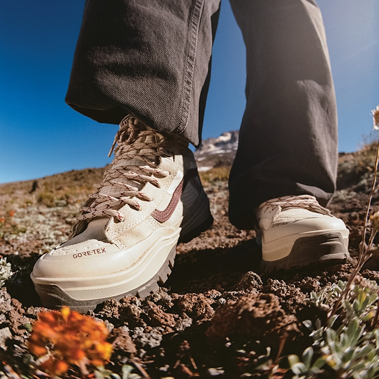 A close-up of someone wearing the red and white Sk8-Hi GORE-TEX and walking on a hillside with blue sky in the background.