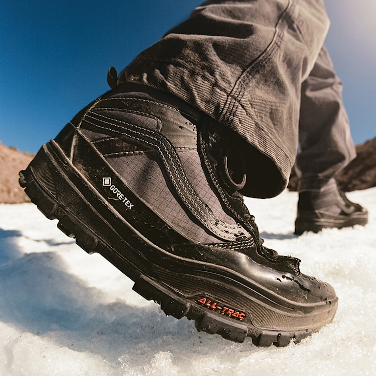A close-up of someone wearing the black Sk8-Hi GORE-TEX and walking on snow with a mountain in the background.
